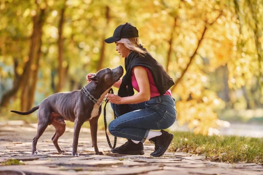 Having a walk. Woman in casual clothes is with pit bull outdoors.