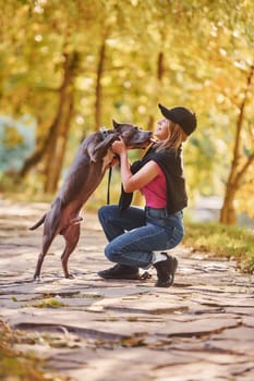 Having a walk. Woman in casual clothes is with pit bull outdoors.