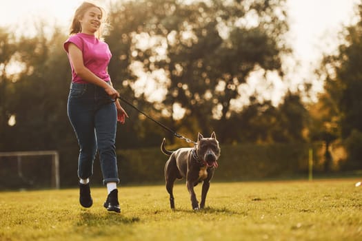 On sportive field. Woman in casual clothes is with pit bull outdoors.