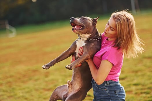 Positive emotions. Woman in casual clothes is with pit bull outdoors.