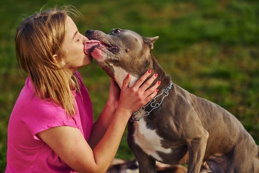 Outdoors on the field. Woman in casual clothes is with pit bull.