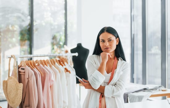 Standing and smiling. Seamstress is in her office that is with different clothes.