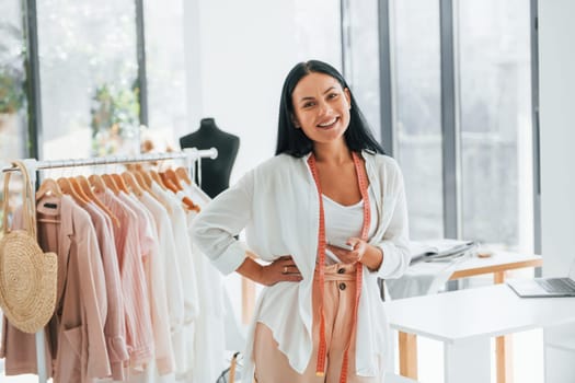 Standing and smiling. Seamstress is in her office that is with different clothes.