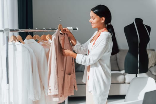 Seamstress is standing in her office that is with different clothes.