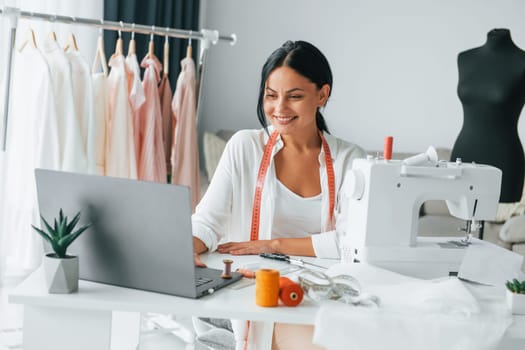 White colored sewing machine. Seamstress is in her office that is with different clothes.