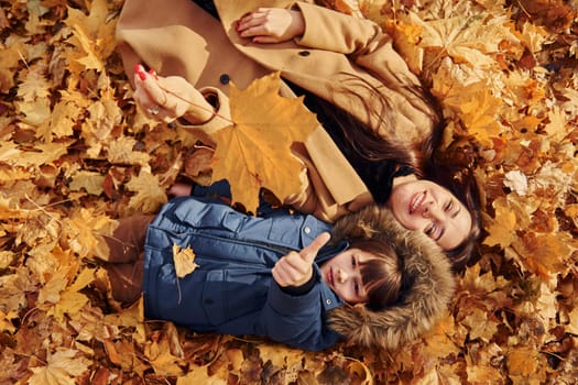 Laying down on the leaves. Mother with her son is having fun outdoors in the autumn forest.