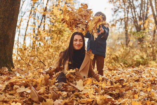 Beautiful nature. Mother with her son is having fun outdoors in the autumn forest.
