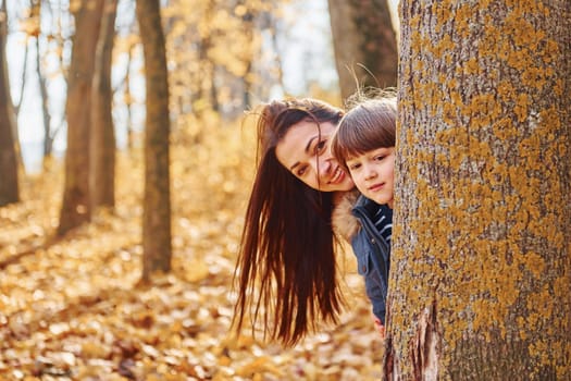 Beautiful nature. Mother with her son is having fun outdoors in the autumn forest.