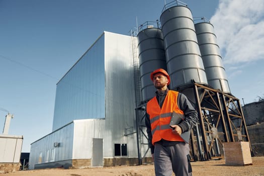 Building exterior. Construction worker in uniform is outdoors near the factory.