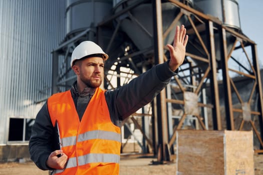 Showing stop gesture. Construction worker in uniform is outdoors near the factory.