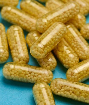 Transparent medical capsules with yellow granules inside on a blue background, tablets for treatment, vitamins