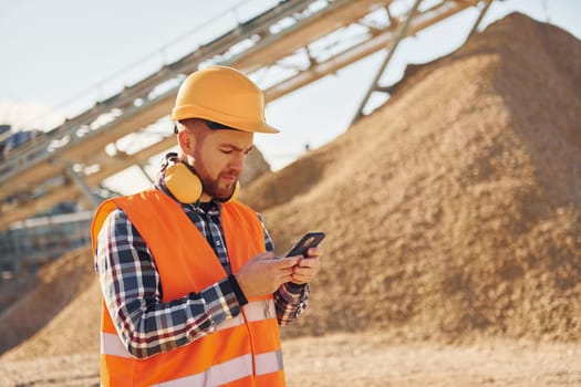With yellow headphones on neck. Construction worker in uniform is on the quarry.