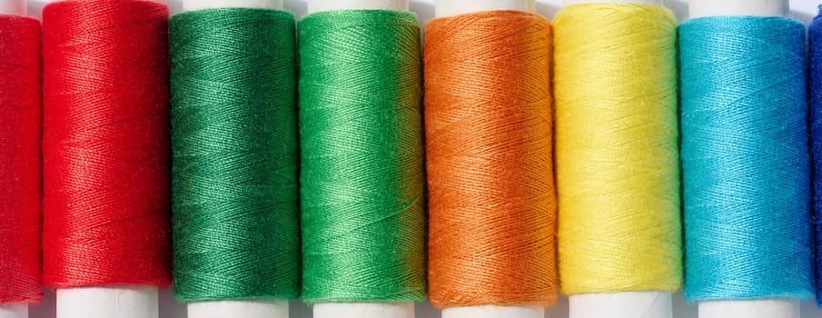 Multicolored spools of sewing threads on a white background, top view