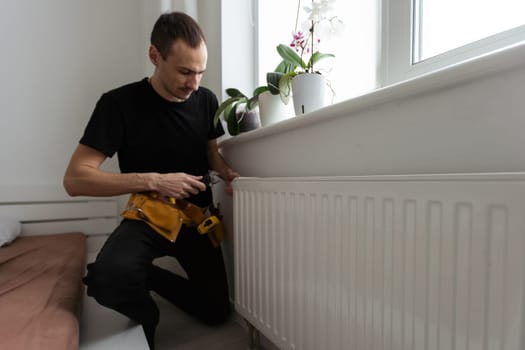Man is repairing radiator battery in the room. Maintenance repair works renovation in the flat. Heating restoration. Wrench in hands. High quality photo