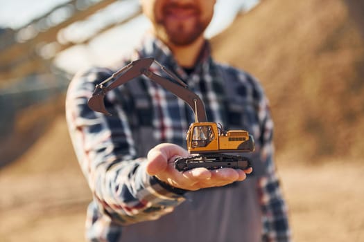 Holding toy. Construction worker in uniform is on the quarry.