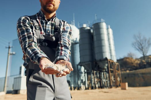 Holding soil. Construction worker in uniform is outdoors near the factory.