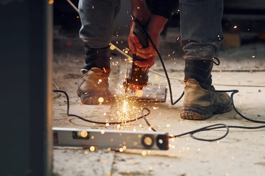 Close up view of man's legs and hands with slicing tool. Working with metal.