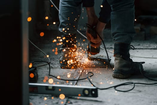 Sparks flying. Close up view of man's legs and hands with slicing tool. Working with metal.