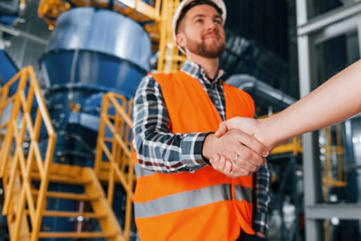 Making handshake with customer. Construction worker in uniform is in the factory.