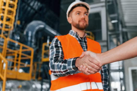 Making handshake with customer. Construction worker in uniform is in the factory.