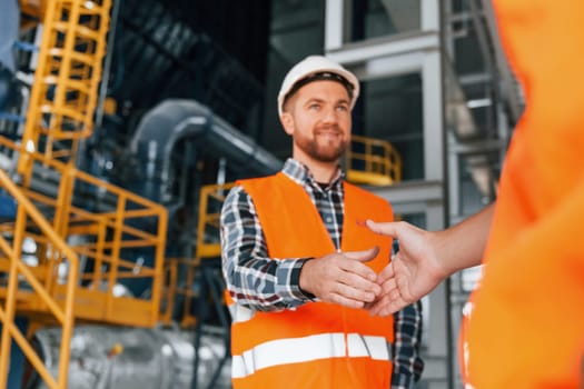 Making handshake with customer. Construction worker in uniform is in the factory.