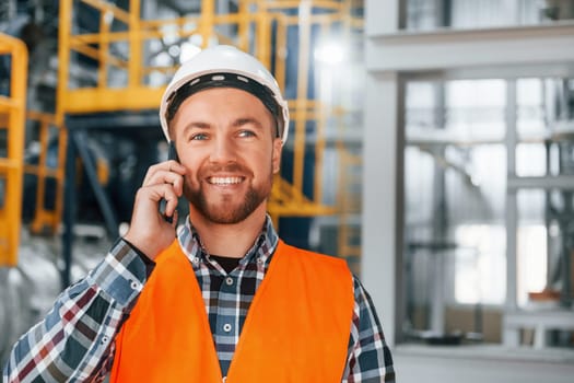 Talking by phone. Construction worker in uniform is in the factory.