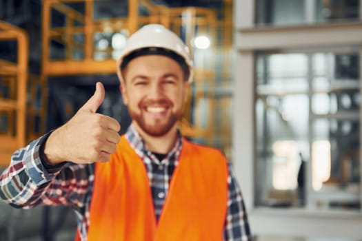 Posing for camera. Construction worker in uniform is in the factory.