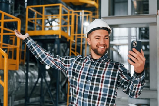 Holding phone. Construction worker in uniform is in the factory.