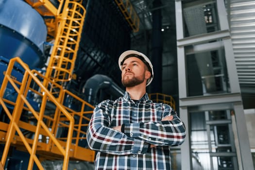 Standing with arms crossed. Construction worker in uniform is in the factory.