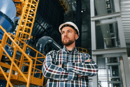 Standing with arms crossed. Construction worker in uniform is in the factory.