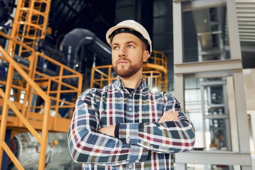 Standing with arms crossed. Construction worker in uniform is in the factory.