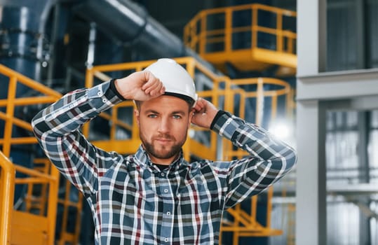 In white hard hat. Construction worker in uniform is in the factory.