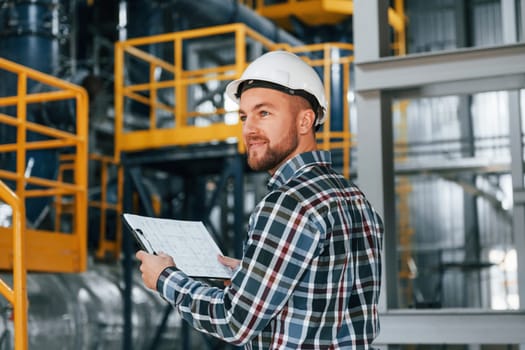In white hard hat. Construction worker in uniform is in the factory.