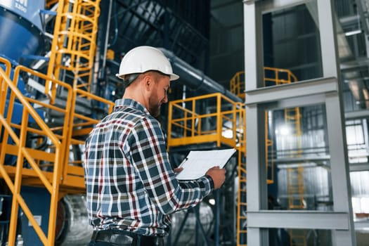 In white hard hat. Construction worker in uniform is in the factory.