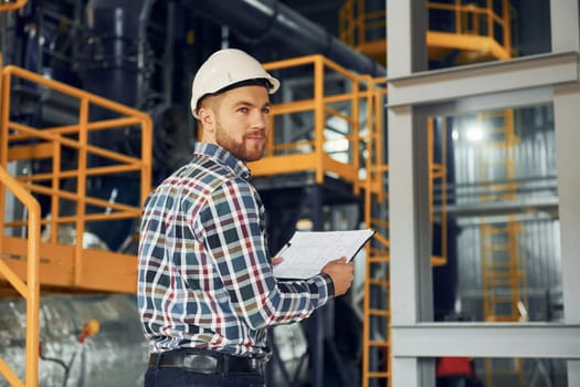 Engineer is indoors. Construction worker in uniform is in the factory.