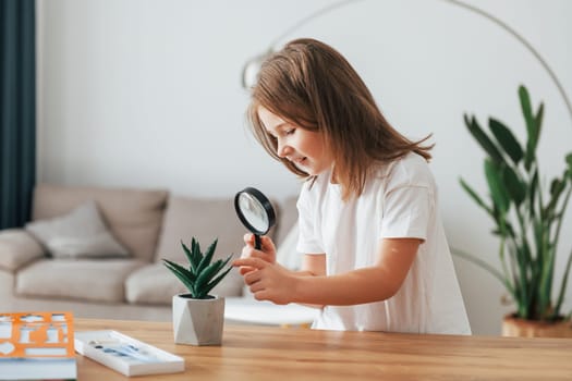 Little girl is sitting by the table with magnifying glass.