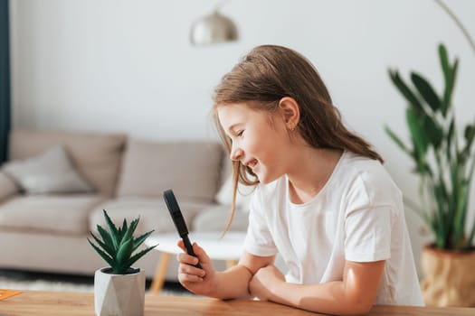 Little girl is sitting by the table with magnifying glass.