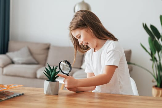 Little girl is sitting by the table with magnifying glass.
