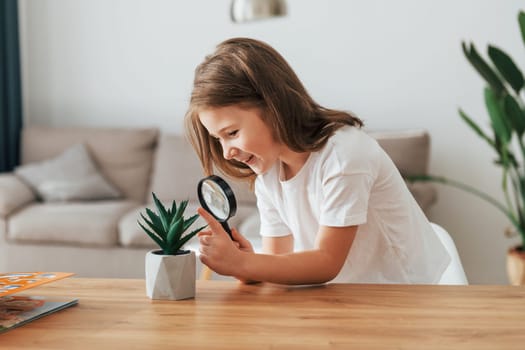 Little girl is sitting by the table with magnifying glass.