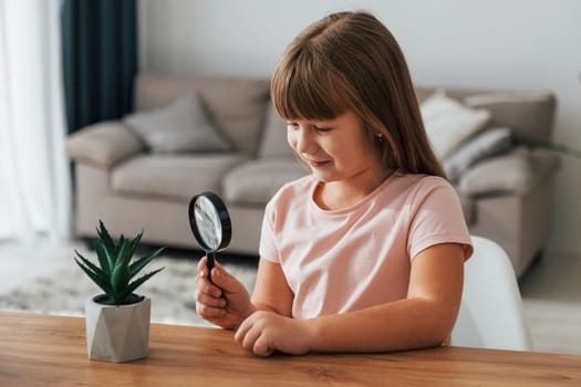 Little girl is sitting by the table with magnifying glass.
