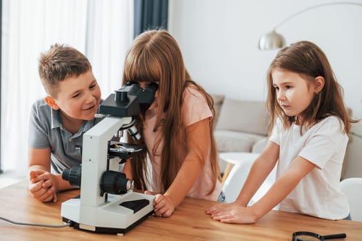 Using microscope. Kids having fun in the domestic room at daytime together.