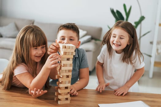 Jumbling tower game. Kids having fun in the domestic room at daytime together.