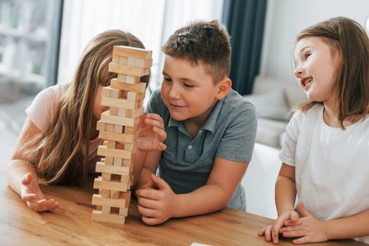 Focused on the jumbling tower game. Kids having fun in the domestic room at daytime together.