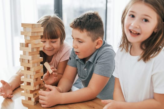 Focused on the jumbling tower game. Kids having fun in the domestic room at daytime together.