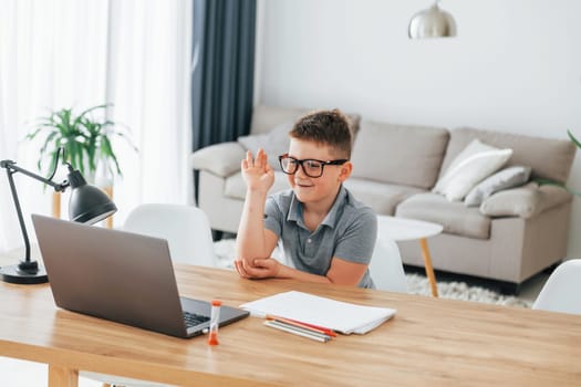 Raised up his hand. Little boy is having online lessons by using laptop at home.