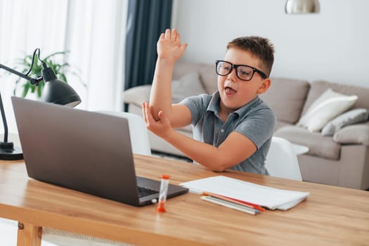 Raised up his hand. Little boy is having online lessons by using laptop at home.