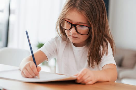 Little girl is sitting by the table and learning to draw.