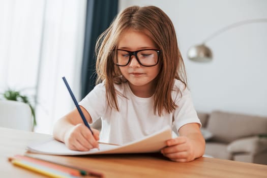 Little girl is sitting by the table and learning to draw.