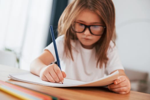 Little girl is sitting by the table and learning to draw.