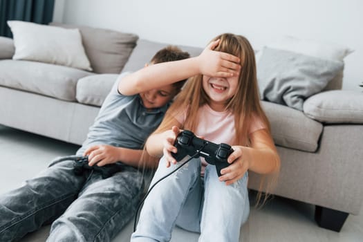 Sitting on the floor and playing videogame. Kids having fun in the domestic room at daytime together.